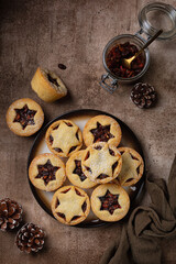 Brown food table with Traditional british christmas Mince pies on a brown plate, sprinkled with sugar. Also called mincemeat or fruit pie, filled with a mixture of fruit, spices and suet.