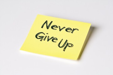 A yellow sticky note displays the motivational message Never Give Up with bold, hand-drawn black lettering on a plain, bright background.