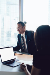 Fototapeta premium Group of business people sitting at office desktop with laptop with blank screen area for advertising text collaborating and brainstorming togetherness, intelligent colleagues cooperating indoors