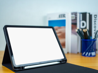 Tablet with blank screen on wooden table. Office supplies, Books on wooden table and white wall. Space for copying your text, Workspace and copy space, Desk with office supplies.