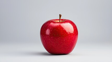 A shiny red apple sits on a simple background, highlighting its vibrant color and smooth surface.