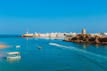 A scenic view of Sur Oman with traditional boats on tranquil waters beneath a clear blue sky