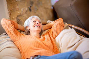 Senior woman smiling and relaxing on a couch with arms behind her head