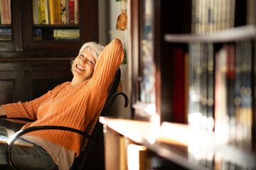 Elderly woman relaxing in cozy home library with sunlight