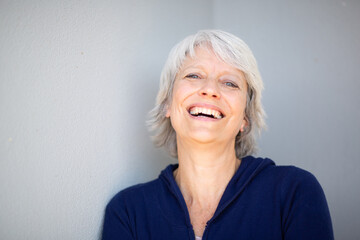 Smiling mature woman leaning against gray wall