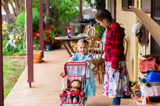 Two little aussie girls pushing dolly in pram on back verandah of Australian home