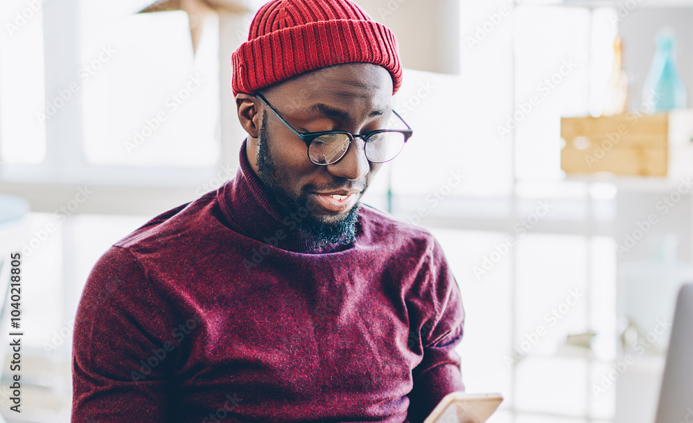 Poster african american hipster guy in spectacles sending text message on mobile phone while working online