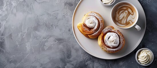 Plate with cinnamon buns cream and a cup of coffee on a textured grey background with space for text or design copy space image