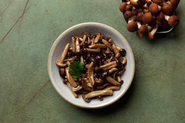 Sautéed honey fungus or Chiodino or stamp edible mushrooms in a black plate with autumn leaves on a green table.