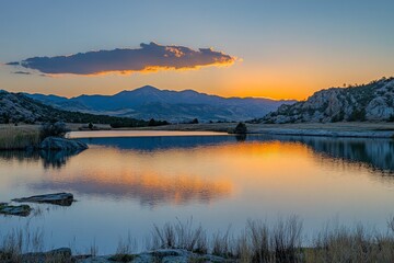 A peaceful sunset scene with orange hues reflecting over a calm lake surrounded by mountains, creating a tranquil and serene atmosphere filled with natural beauty.