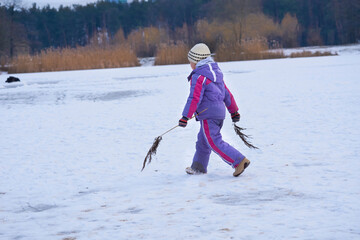 Playful child girl walks on a frozen lake in a winter forest park