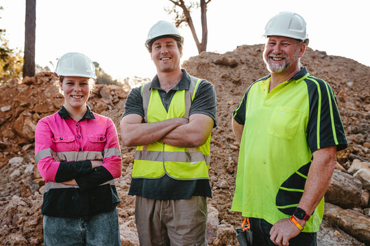 Three construction workers standing wearing safety equipment on the worksite with arms crossed