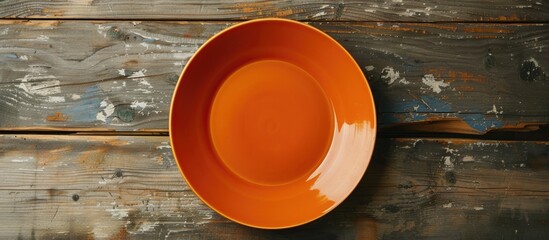 A plain orange plate is set against a wooden surface from a top view with ample copy space visible