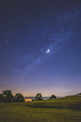 Fototapeta premium A night sky with stars and a crescent moon over a distant horizon