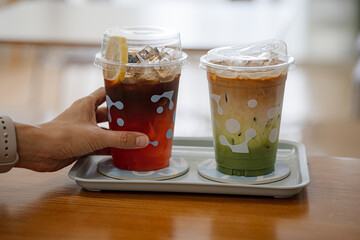 hand of woman holding a take-out iced tea honey lemon on table at coffee shop
