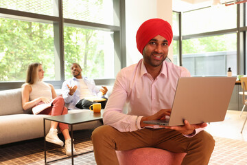 Businessman wearing Sikh turban sitting with laptop in office