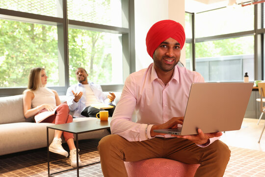 Businessman wearing Sikh turban sitting with laptop in office