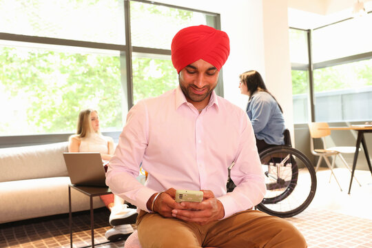 Businessman wearing Sikh turban sitting with phone in office
