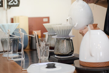 Barista making drip coffee by pouring spills hot water on coffee ground with prepare filter from copper pot to glass transparent chrome drip maker on wooden table in cafe shop