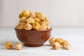Clay bowl overflowing with physalis fruits on light table