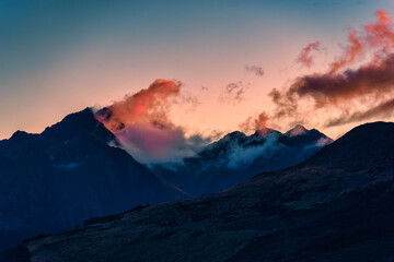 Mountain peak at sunset with colorful clouds flowing through