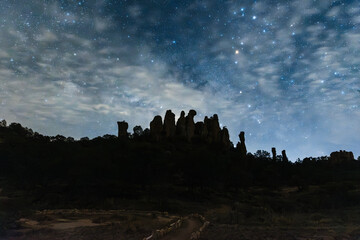 Paisaje sereno de montañas y formaciones rocosas, al anochecer, bajo un cielo lleno de estrellas,...