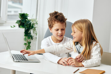 Happy Caucasian boy and girl sitting at a table in their cozy living room, engrossed in their online studies on laptops With headphones on, they are fully concentrated on their elearning, typing and