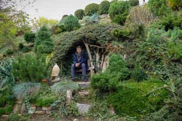 boy sits in a decorative gazebo on a green slope, bushes, stones, plants, landscape