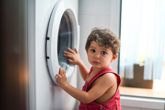 Little baby looking washing machine at home - Powered by Adobe