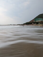 A serene evening at Rushikonda Beach, in Andhra Pradesh, India, with soft golden hues from the setting sun reflecting on the calm, blue waters.
