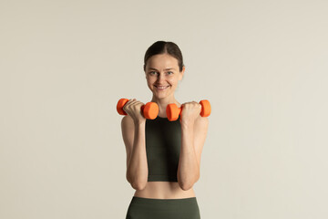 A fit woman dressed in dark activewear holds bright orange dumbbells, showcasing her enthusiasm for...