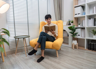 Young Man Sitting Comfortably in a Modern Living Room Reading a Book on a Bright Yellow Chair