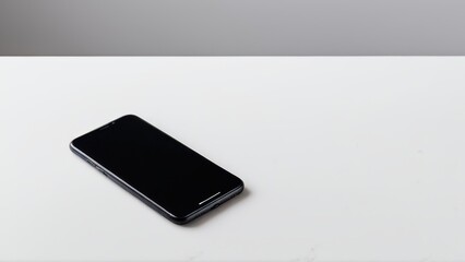 Fototapeta premium A sleek smartphone with a blank white screen stands upright on a plain surface against a minimalist gray background, emphasizing modern design aesthetics.