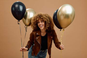 Happy multiracial woman holding golden and black coloured balloons and looking away.