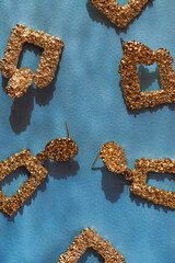 Creative composition made of golden earrings on blue sunlit background with shadows. Beauty and fashion concept