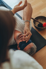 A man lying on a mat with a blindfold, practicing breathing exercises while a woman acts as a...
