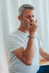 A man sitting in lotus position, practicing alternate nostril breathing exercises during a...