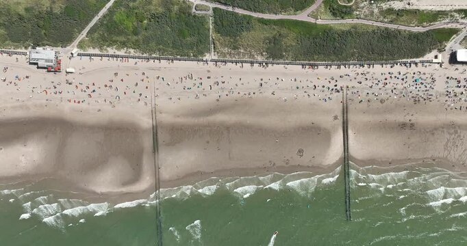 Drone view of a busy beach with green field and sea waves on a sunny day in Domburg, Netherlands