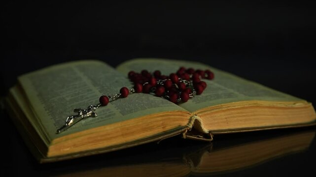 An open Bible with rosary in the dark in the light of fire on background