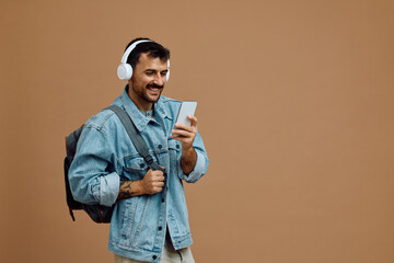 Fototapeta premium Studio shot of man with backpack listening music on headphones and using smart phone.
