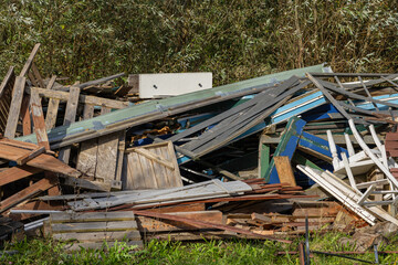 Pile of old wooden boards and discarded furniture parts in a grassy area on a sunny day. Concept of...