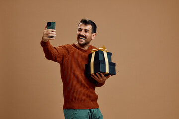 Studio shot of happy man with black golden gift boxes taking selfie.