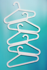 Top view minimal style pattern of white plastic hangers with hooks on teal background. Flatlay with Clothes racks for hanging garments. Minimal trend photo, lifestyle or interior design content