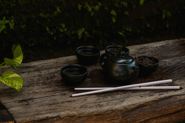 A small black teapot with a Japanese tone with the glass is arranged on an antique wooden table