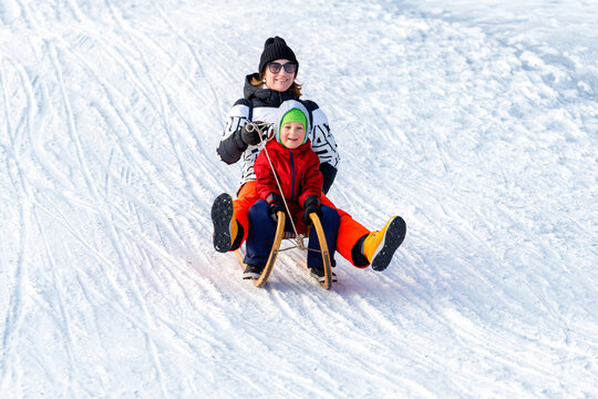 Young adult mother with cute baby boy son enjoy have fun sledging downhill at frozen white snow hill woods forest park landscape bright sunny cold winter day. Outdoors winter season family activity