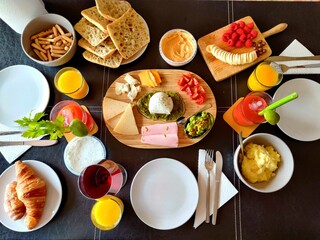 FULL BREAKFAST SEEN FROM ABOVE FOR THREE PEOPLE WITH BREAD, CHEESE, HAM, ORANGE JUICE, COCKTAIL, HUMMUS, FRUIT. BANANA, RASPBERRY, WINE, AVOCADO