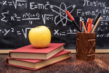  Vuelta a la escuela con libros, lapicero y manzana con fondo de pizarra escrita con fórmulas de física y matemáticas © KukiLadrondeGuevara