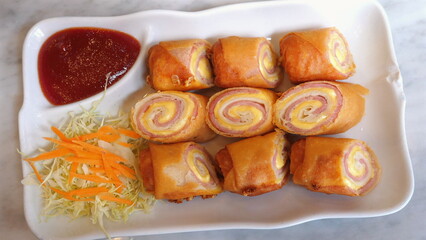 Close-up of delicious crispy spring rolls with vibrant dipping sauce and fresh shredded vegetables, beautifully presented on white plate. Appetizing Asian Cuisine.