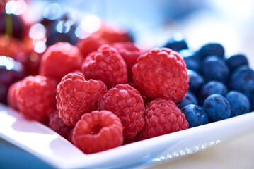 Fresh raspberries and blueberries on a white plate, on a blurred background. close-up.
