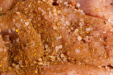 a salted piece of fresh chicken meat on paper sprinkled with spices